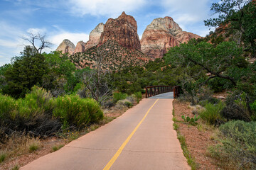 Recreational asphalt path in Zion National Park leading towards a rustic bridge over the Virgin River, outdoor recreation, arid desert climate
