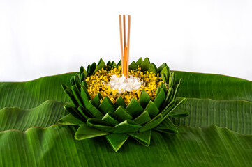 Krathong that have 3 incense sticks and candle decorates with white and yellow flowers puts on banana leaf for Loy Krathong festival on white background.