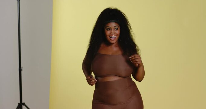 After camera cue African American woman laughing smoothing shapewear dancing on backdrop in studio