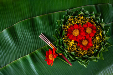 Krathong decorates with flowers that have blurred focus of 3 incense sticks and candle put on banana leaf for Loy Krathong festival.