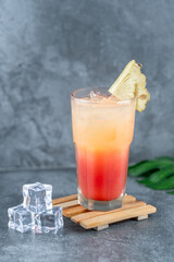 Tropical mocktail with pineapple garnish, vibrant layers of orange and red, served over ice. Refreshing summer drink perfect for parties and food menus.