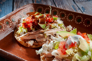 Typical Mexican food called ANTOJITOS, chicken tostadas with lettuce, tomato, spicy salsa fresh cheese, and cream, served on a handmade M,exican clay plate, macro photography