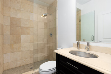 A bathroom with a dark wood vanity cabinet with a brown countertop, stainless steel sink, and a shower with brown tiles and glass door.