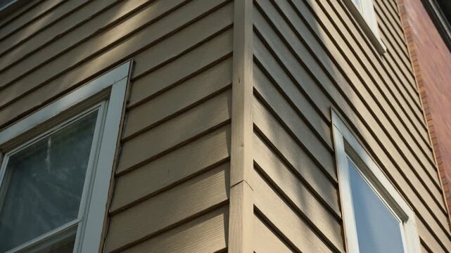 Close-up of old residential building exterior, corner of house with worn wooden siding and aged windows. Peeling paint and weathered frames highlight the need for renovation