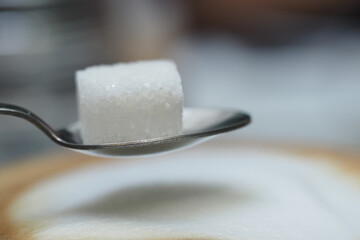 Sugar cube balanced on a spoon above smooth white surface