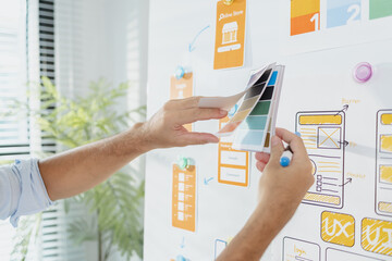 A young designer is working on a UX UI project, analyzing mobile app wireframes and choosing color...