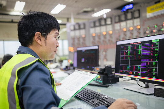 Engineer monitoring SCADA system in control room and documents, analyzing power grid operations on dual screens, energy management, automation, smart grid, and system supervision Concept
