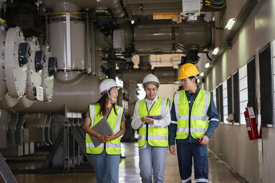 teamwork and industrial safety, Group of engineers and technicians wearing safety helmets and reflective vests inspecting high-voltage gas-insulated switchgear (GIS) inside a power plant