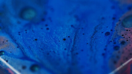 Paint spilling. Round drop. Defocused blue golden purple color sparkling oil water liquid fluid floating on abstract art background.
