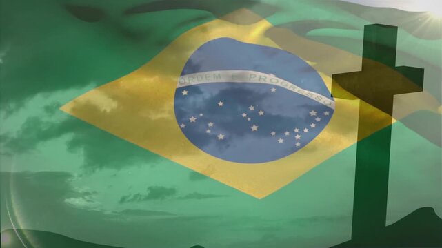 Gentle breeze making Brazilian flag fluttering showing stars and motto over green sky beside cross