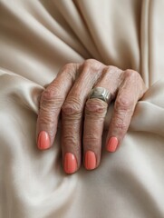 Elegant Hand with Coral Nails and Geometric Ring on Satin