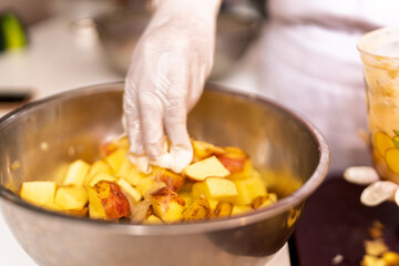 Chef preparing diced potatoes for frying in a bowl