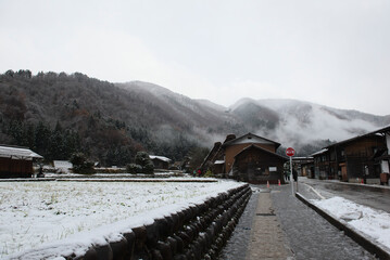 Shirakawa-go, Gifu, Japan, A beautiful winter landscape featuring a traditional Gassho-zukuri style farmhouse covered in the first snow of the season, surrounded by misty mountains.