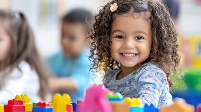 A young girl with curly hair playing with colorful building blocks in a classroom setting.