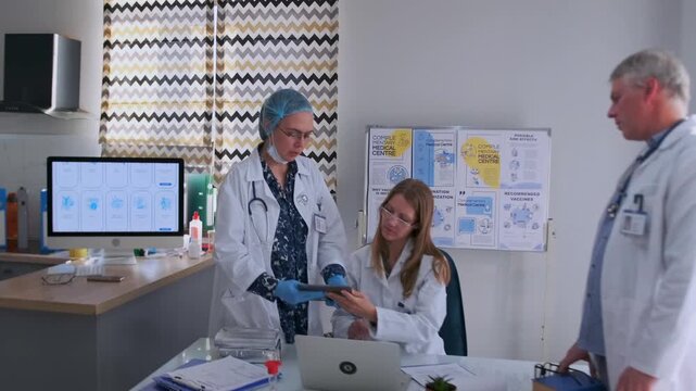 Three doctors in white coats collaborate in clinic office, reviewing medical records with tablet and laptop. Healthcare professionals discussing diagnosis and treatment in teamwork setting. - Powered by Adobe