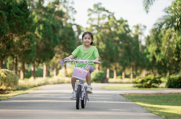 Fototapeta premium Happy young girl riding bicycle in park during sunny day, enjoying childhood and outdoor activities in nature, healthy lifestyle and joy of movement