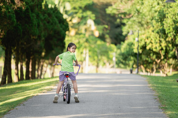 Obraz premium Young girl riding bicycle in park, enjoying sunny day, smiling with joy, greenery surrounding, outdoor activity, childhood fun, carefree moments