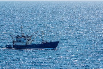 Fishing boat in blue sea and clear sky with birds flying overhead.