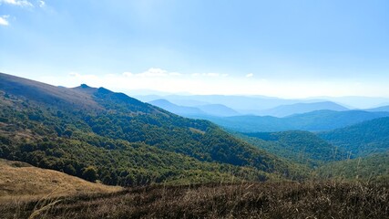 Scenic panoramic view from the Bieszczady Mountains in Poland, showing layers of green forested ridges fading into a blue atmospheric haze.

