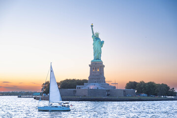 Sailboat passing Statue of Liberty at sunset in New York Harbor with dramatic sky © Kevin