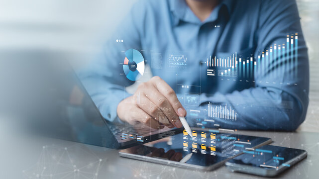 Businessman analyzing financial data and digital charts on tablet and laptop, representing data analytics, business intelligence, finance, and digital economy.