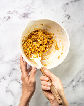 Mixing apple caramel pie filling &mdash; diced apples, caramel, and spices in a large bowl with hand stirring by spatula. Marble background, high key style.