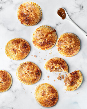 Freshly baked apple, caramel, and cardamom hand pies &mdash; crisp pastries on marble with oozing caramel filling and spoon of sauce, bright high key background, copy space.