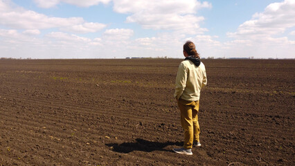 A solitary man stands in a vast, empty field, looking out at the horizon under a wide, cloudy sky,...