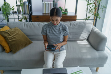 Asian women using calculator calculating Monthly expenses
And Working With Laptop at home