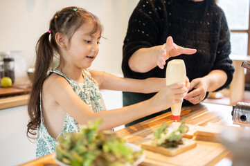 Asian daughter squeezed mayonnaise on bread making sandwich aside mother at kitchen cooking counter.