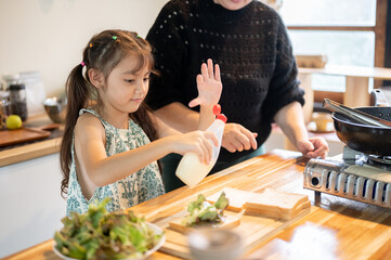 Asian daughter holding mayonnaise over bread making sandwich with mother at kitchen cooking counter.