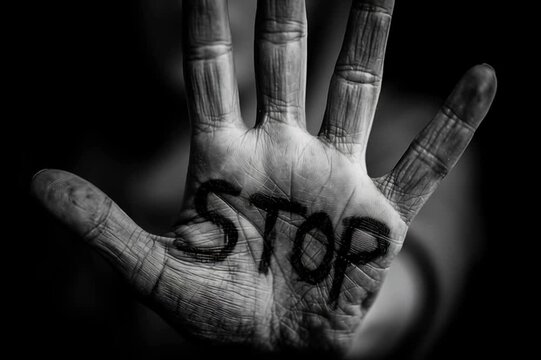 female a black and white photo of female open hand with the word "STOP" written with black sharpie on the inside of the palm. dark gray background.