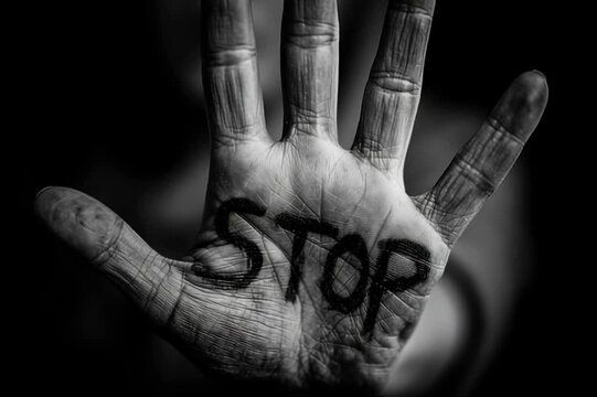 female a black and white photo of female open hand with the word "STOP" written with black sharpie on the inside of the palm. dark gray background.