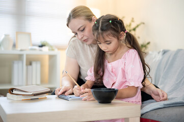 Caucasian mother looking at kid daughter writing doing homework at table aside sofa in a living room