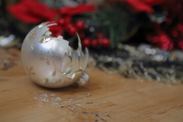The shards and remnants of a broken Christmas bell ornament are shown on the floor next to colorful holiday tree decorations.