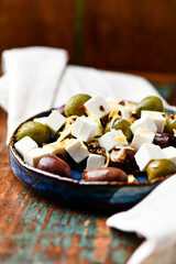 Green and kalamata olives and feta cheese on rustic wooden background. Soft focus.	