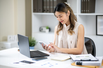 Fototapeta premium Pretty woman office worker holding and looking at a calculator aside laptop at white table in office