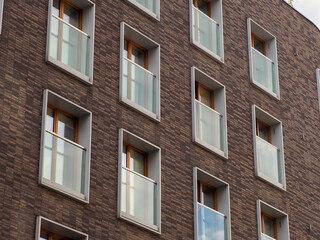 Fototapeta premium A close-up of a modern brick facade with multiple large windows and glass balconies on a residential building.