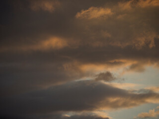 A horizontal shot of the sky at sunset, with heavy dark clouds mixed with bright orange and golden tones.