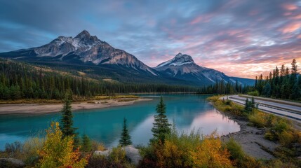 A turquoise river winds through a lush forest with snow-capped mountains in the background under a colorful, dramatic sunrise sky