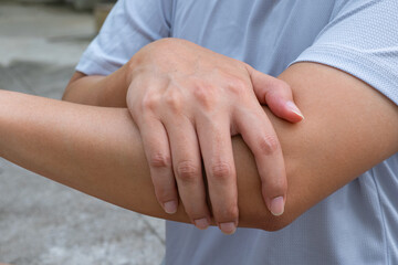 Asian male clutching outer elbow in visible discomfort—suggesting acute lateral epicondylitis or strain post-activity, ideal for orthopedic care ads.