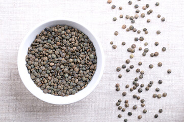 Puy lentils in a white bowl on linen. Dried variety of small lentils, mottled, of slate-gray to...