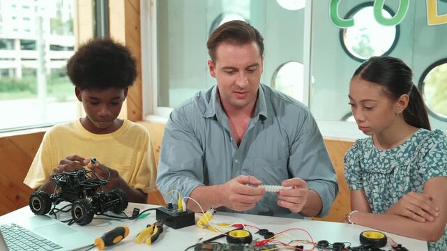 Smart mentor teaching about electronic equipment while fixing car model. Caucasian teacher pointing while explain robotic construction at table with laptop, car model scatter around. Edification