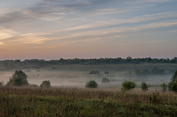 Naklejka premium Hilly plain covered in fog, illuminated by the dawn sun.