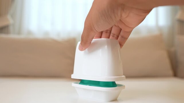 Lifting the lid of a gel air freshener at home represents caring for air quality, enhancing mood, daily cleanliness, easy maintenance, and creating a welcoming, comfortable atmosphere.
