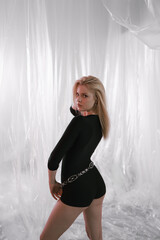 A gorgeous girl in a black tight-fitting suit with a stylish belt on a delicate airy background.