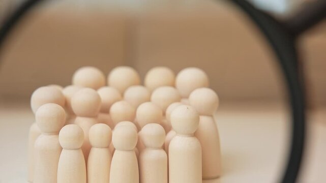 A magnifying glass focuses on a group of wooden people, symbolizing government surveillance, social development, community analysis, public policy, human behavior studies, and collective identity.
