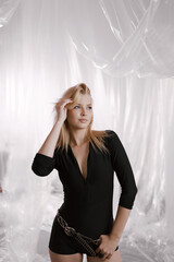 A gorgeous girl in a black tight-fitting suit with a stylish belt on a delicate airy background.