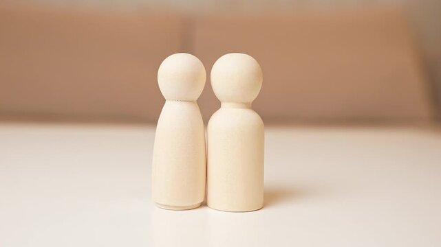 Hands hold two separated heart halves in front of male and female wooden figures, symbolizing breakup, separation, lost connection, emotional distance, heartbreak, and the end of a relationship.

