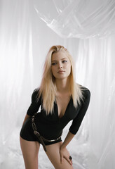 A gorgeous girl in a black tight-fitting suit with a stylish belt on a delicate airy background.